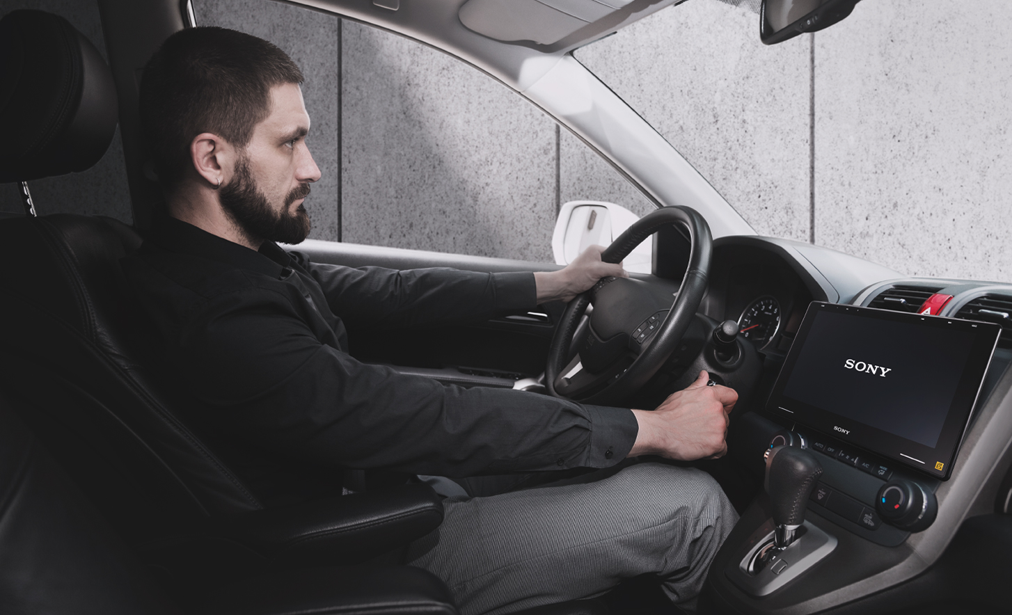 Zdjęcie osoby przekręcającej kluczyk w stacyjce i deski rozdzielczej z radiem samochodowym XAV-9550ES wyświetlającym logo Sony